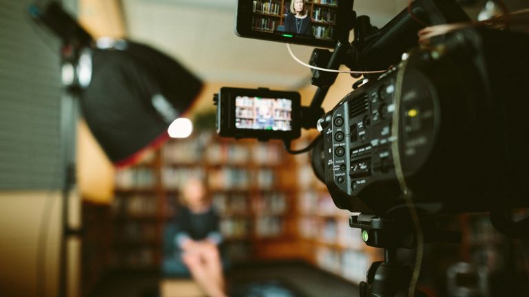 TV camera in foreground, woman seated unfocused in background