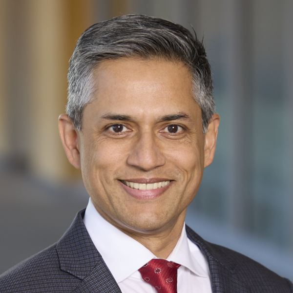 man with gray hair wearing blue suit jacket, white shirt, red tie, smiling