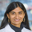 head and shoulders of woman with long dark, straight hairs gold earrings, whitecoat
