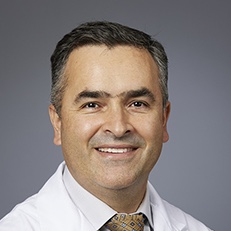 head and shoulders of man wearing whitecoat short dark hair smiling