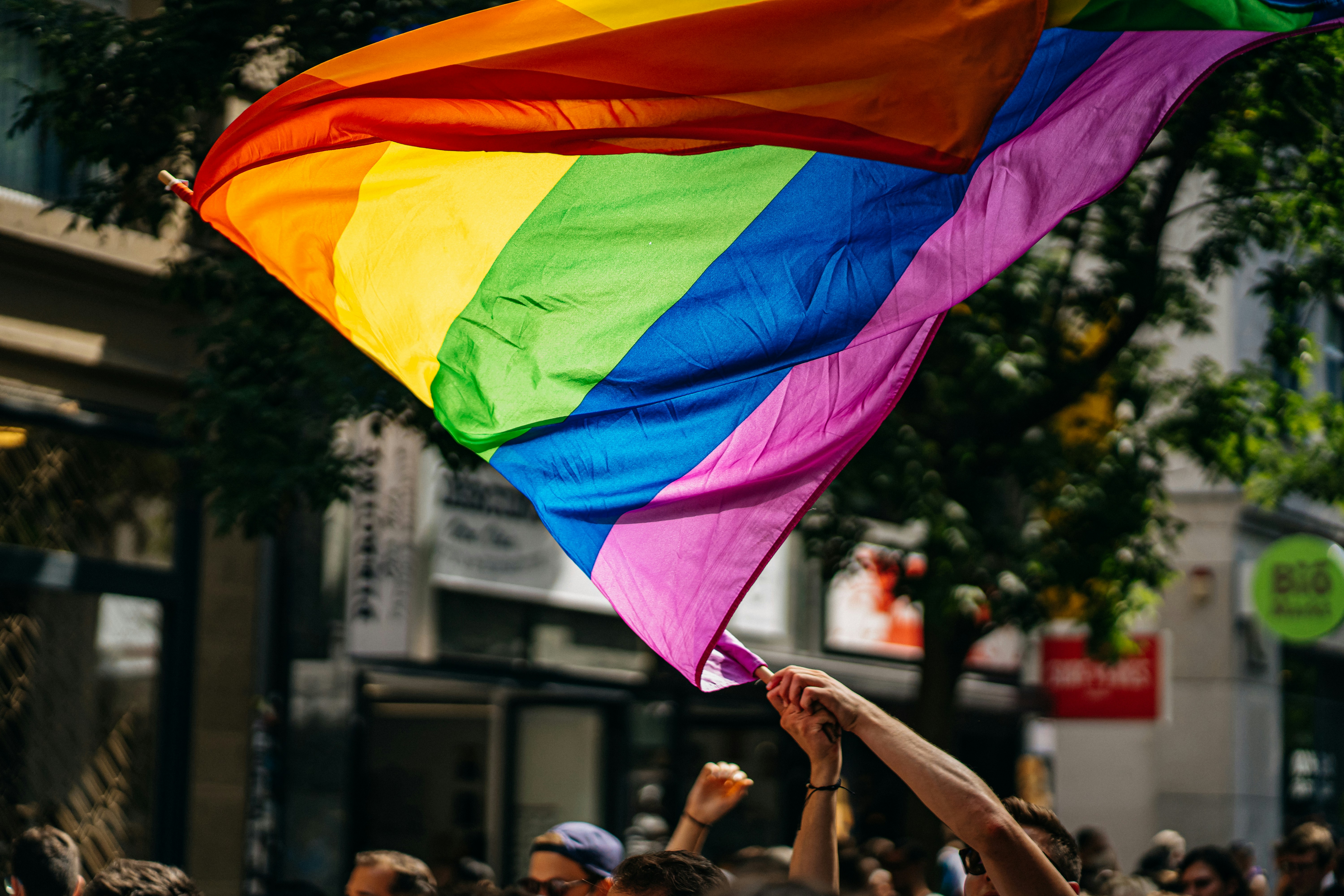 Rainbow flag blowing in wind being held by hands
