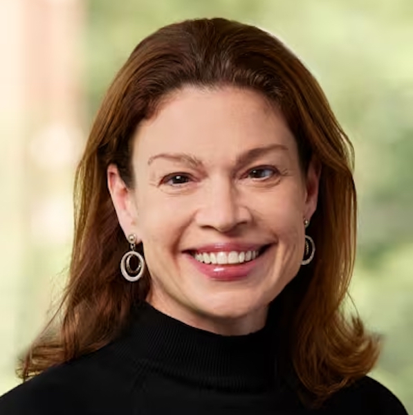 Head shot of woman with shoulder length brown hair black turtleneck sweater, earrings, smiling broadly