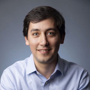 Man with dark short hair smiling wearing open light colored dress shirt