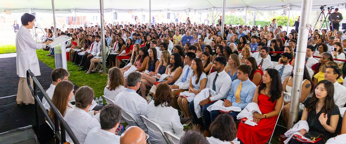 woman at podium in whitecoat addressing students at whitecoat ceremony