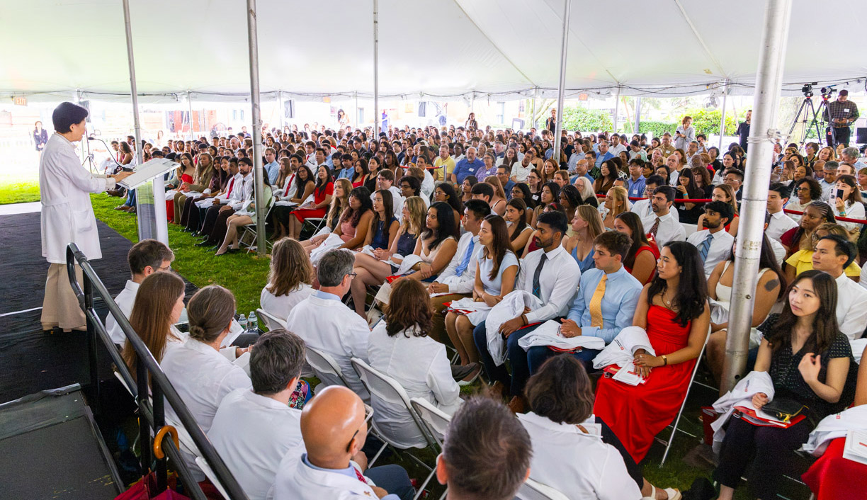 woman at podium in whitecoat addressing students at whitecoat ceremony