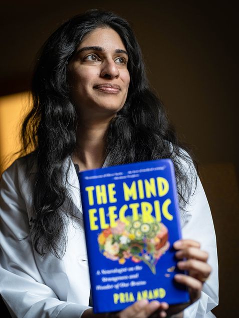 Woman with long dark hair holding a book titled The Mind Electric