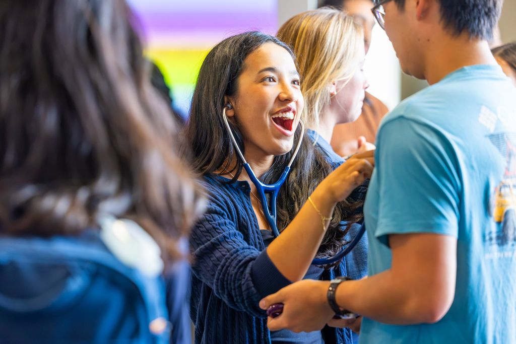 Woman with stethoscope smailing broadly while listening to heartbeat of another person