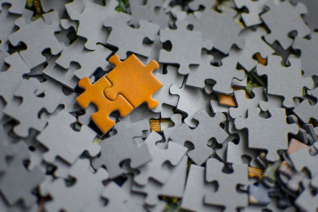 Two interlocking mustard colored puzzle pieces on top of many scattered gray puzzle piece