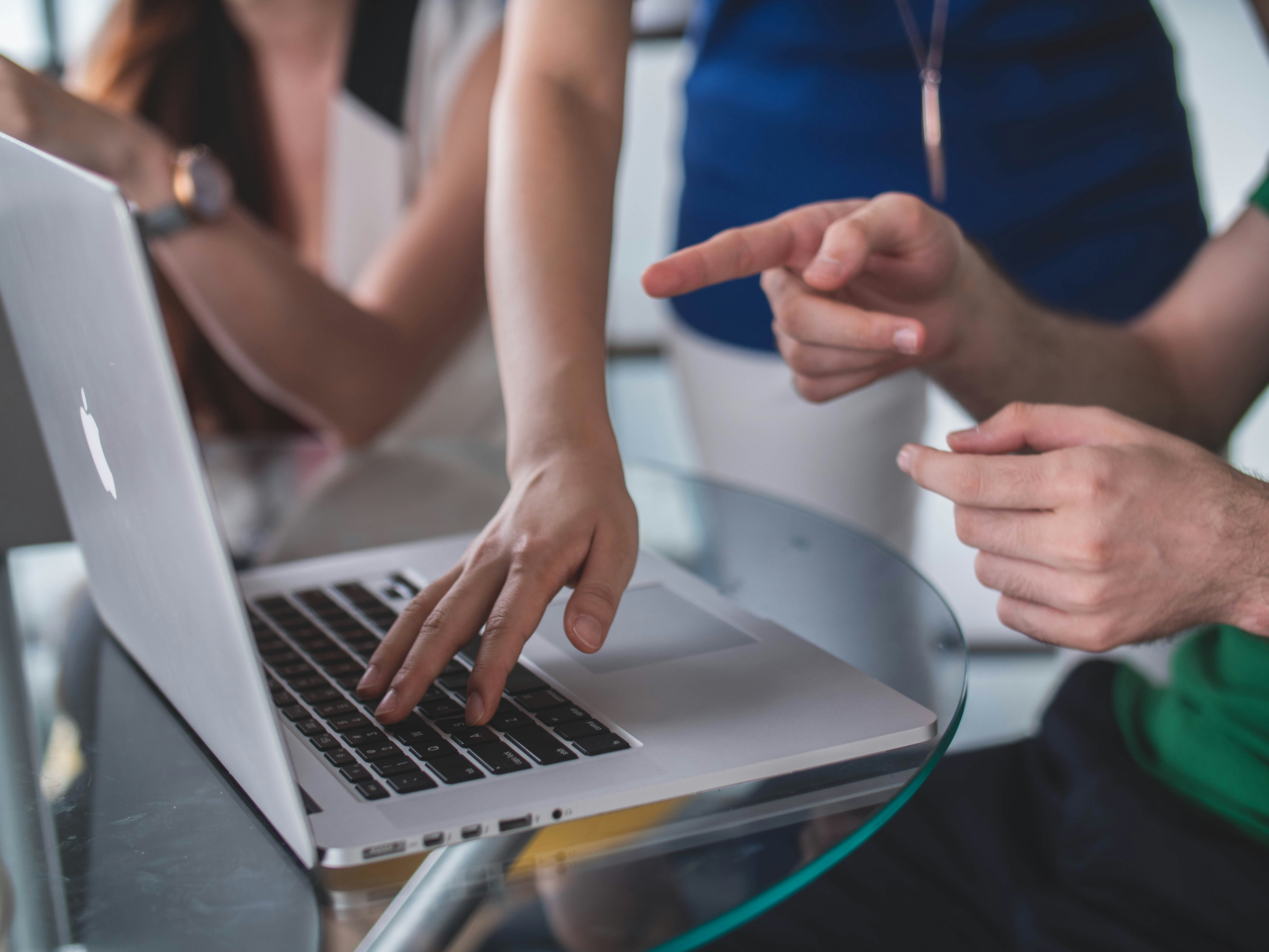 group of people with hands near a silver laptop