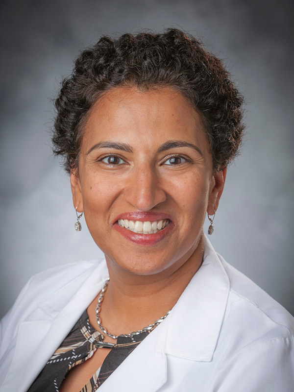 Woman in white coat, dark short hair, smiling broadly