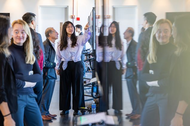 People standing infront of digital screens viewing scientific posters, some of their reflection in screen visible