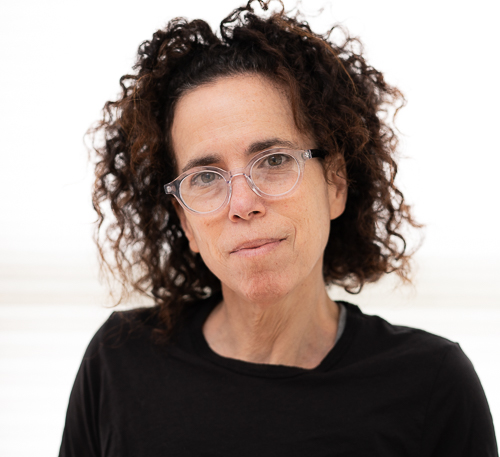 head and shoulders of woman wearing glasses, dark shirt, dark curly hair