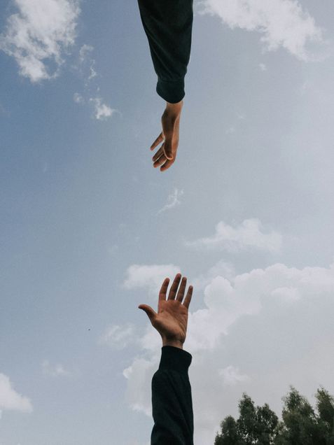 Two hands photographed against a blue sky with clouds