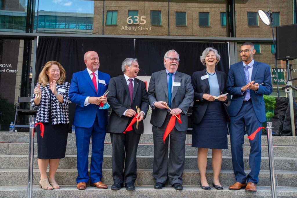 Ribbon cutting on steps of GSDM. Six people all smiling broadly behind red ribbon that had just been cut. Participants from left: Terri Dolan, Dentsply Sirona VP and chief clinical officer, GSDM Dean’s Advisory Board chair David Lustbader (CAS’86, SDM’86), Cataldo Leone, SDM dean ad interim, Robert A. Brown, BU president, Karen Antman, BU Medical Campus provost and School of Medicine dean, and student speaker Justin Middleton (SDM’21, MED’24, SDM’27).