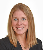 Head and shoulders shot of woman with straight strawberry blond hair smiling broadly wearing a dark suit jacket