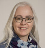 Woman with shoulder length straight white hair, dark rimmed eye glasses wearing blue flowered scarf smiling