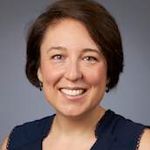 head and shoulders shot of woman with short dark hair wearing dark blue top, smiling