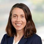 Woman with shoulder length dark brown hair wearing dark blue suit jacket smiling broadly