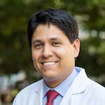 Man with dark hair, wearing white coat, smiling broadly