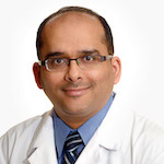 man with eyeglasses, short dark hair wearing white coat