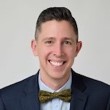 Man with short dark hair blue suit jacket, light blue shirt and bowtie smiling broadly