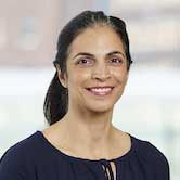 Woman with shoulder-length dark hair pulled back in ponytail, wearing dark top, smiling broadly