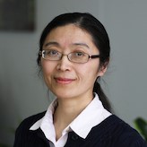 head and shoulders of woman with long dark straight hair in ponytail, eyeglasses, white blouse and dark jacket smiling gently