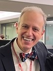 Head and shoulders of man with gray hair wearing dark suit jacket, white shirt, bow tie, smiling broadly