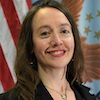 Woman with long brown wavy hair smiling in front of a background of american flag