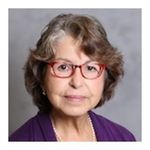 Head and shoulders shot of Mary Tavares short gray/brown hair, red eyglasses, purple suit jacket