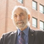 head and shoulders of Myron Allukian outside infront of brick building, gray hair and facial hair gray suit, blue shirt
