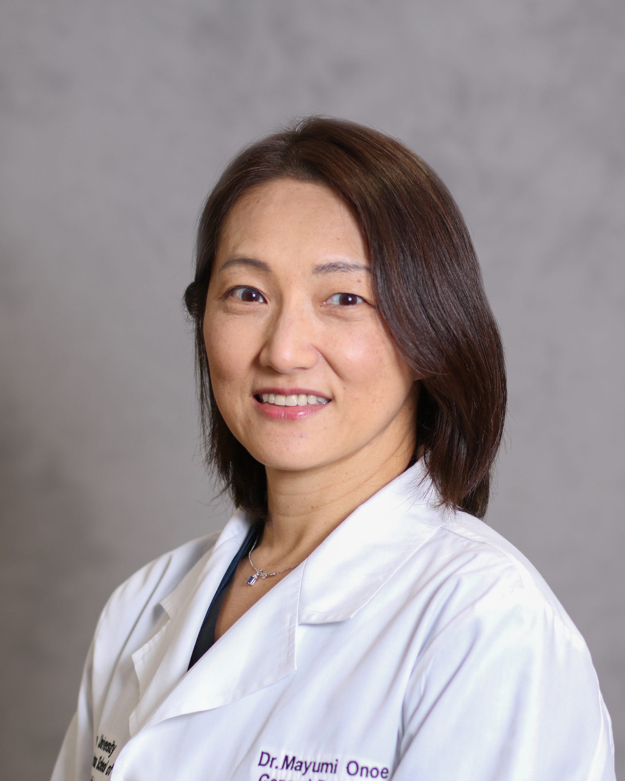 Woman with long straight black hair wearing white coat, smiling