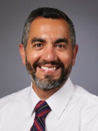 Head and shoulders of Dr. Cruz wearing white shirt with blue/red stripe tie