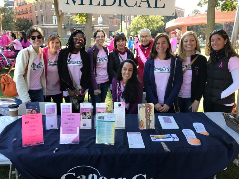 A group of women wearing pink Team BMC T-shirts gather around an info table at the ACS Making Strides event
