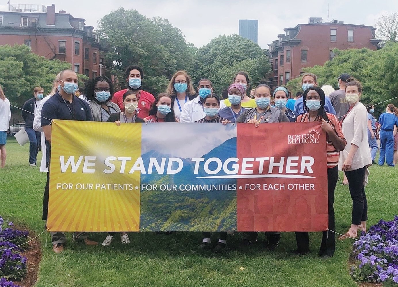 BMC employees wearing masks holding up "We Stand Together" poster at White Coats for Black Lives event